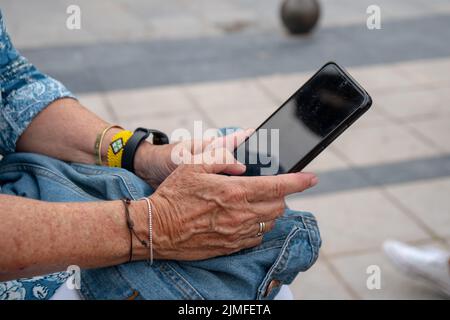Gros plan d'une femme plus âgée avec des bracelets portant un smartphone noir Banque D'Images