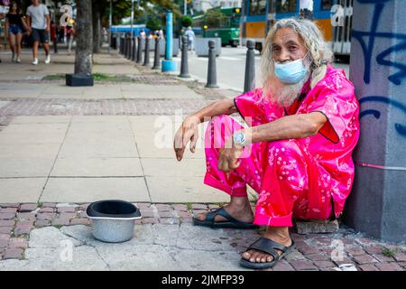 Homme barbu flamboyant avec de longs cheveux blancs et un masque facial portant des vêtements roses propres mendiant pour de l'argent dans les rues de Sofia, Bulgarie, Europe de l'est, Balkans, UE Banque D'Images