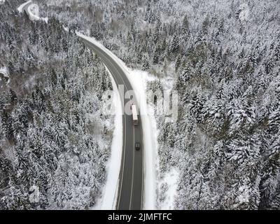Route sinueuse à travers les bois en hiver. Asphalte à travers le col au sommet de la montagne en Roumanie. Banque D'Images