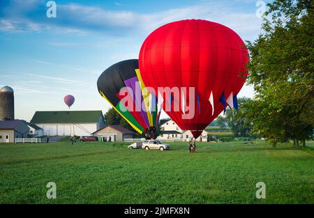 Plusieurs ballons à air chaud débarque dans les terres agricoles, tandis que les amish regardent Banque D'Images