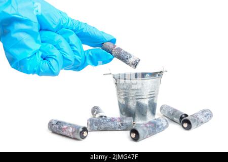 La main gantée jette une batterie à plat fortement corrodée dans un petit seau en acier isolé sur blanc. Concept d'élimination des déchets toxiques. Banque D'Images