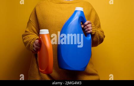 Femme dans un chandail tricoté tient une bouteille en plastique orange et bleu avec du gel de lavage liquide. Linge et corvées, backgro jaune Banque D'Images