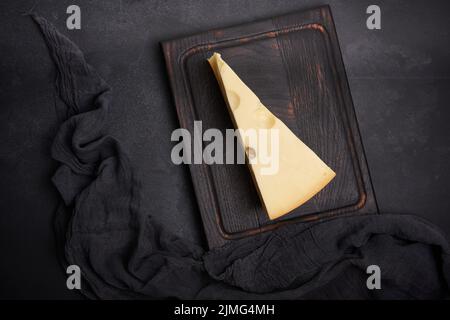 Pièce triangulaire de maasdam sur une planche de bois marron, vue de dessus Banque D'Images