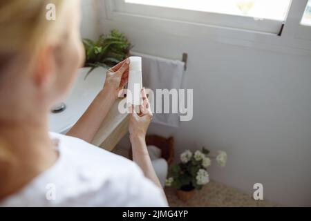 Vue sur l'épaule sur le produit de beauté pour la peau dans les mains de la femme blonde. Gros plan. Arrière. Banque D'Images