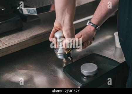 Gros plan sur le barista qui tient le sabotage et presse le café moulu dans le support pour préparer un espresso pour le client Banque D'Images