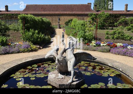 Statue d'une fille et d'un cygne dans un étang de nénuphars dans le jardin clos d'un ancien manoir anglais Banque D'Images