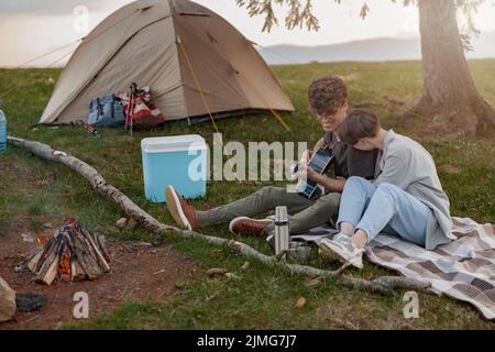 Couple joyeux au camping en montagne. Homme jouant à la guitare pour petite amie. Banque D'Images