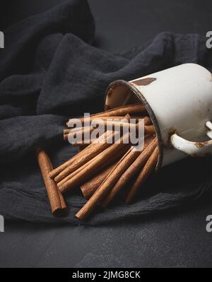 La cannelle se colle dans une tasse en métal ancien sur une table noire. Épice aromatique Banque D'Images