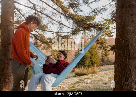 Jeune homme et femme caucasien riant et s'amusant au hamac dans le bois. Heureux ensemble. Banque D'Images