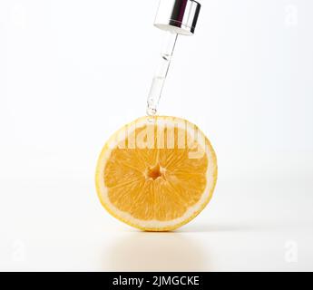 Pipette en verre avec une goutte, à côté d'un demi citron sur fond blanc. Acides de fruits dans les cosmétiques Banque D'Images