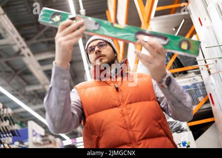 un homme choisit un niveau de bulle de construction dans un magasin de matériaux de construction et d'outils Banque D'Images