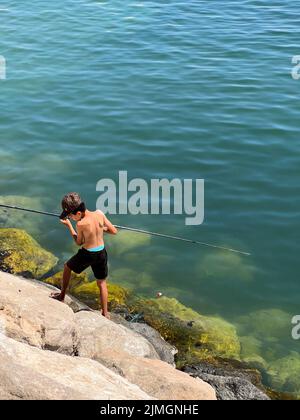 Jeune enfant pêcheur. Pêche pour enfants sur la rive de la rivière,  activités de loisirs en plein air en été. Petit garçon sur la rive de la  rivière avec la canne. Orientation