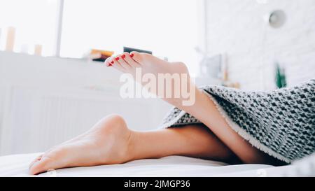 Hygiène des pieds. Femme pieds nus couchée sur un lit. Des jambes magnifiques qui sortent de la couverture. Banque D'Images