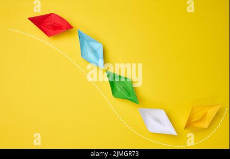 Les bateaux en papier multicolores suivent la ligne de repère sur fond jaune. Le concept de manipulation des masses, le chemin d'un St Banque D'Images