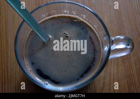 Un délicieux café noir frais est servi dans une tasse en verre et placé sur une table en bois. Banque D'Images