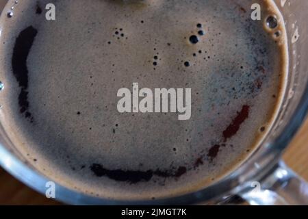 Un délicieux café noir frais est servi dans une tasse en verre et placé sur une table en bois. Banque D'Images