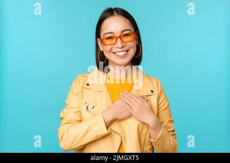 Portrait de femme asiatique souriant, tenant les mains sur le coeur et regardant avec tendresse, attention à la caméra, émotion reconnaissante, debout Banque D'Images