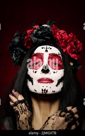 Portrait d'une belle femme avec un maquillage de crâne de sucre avec une couronne de fleurs sur sa tête, fond rouge Banque D'Images