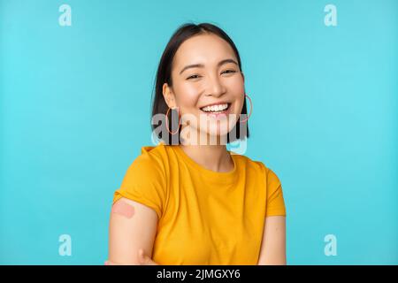 Campagne de vaccination de Covid-19. Bonne et saine fille asiatique riant après la vaccination du coronavirus, bandaid sur l'épaule, W Banque D'Images