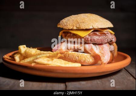 Hamburger de bœuf grillé de qualité supérieure avec bacon, fromage et frites. Délicieux hamburger américain sur fond de bois. Banque D'Images