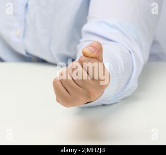 Main féminine pliée dans un poing sur une table blanche. Leader strict, agression et pression sur la personne Banque D'Images