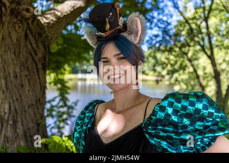 Cottbus, Allemagne. 06th août 2022. Un visiteur du festival d'Elbenwald se tient près d'un étang dans le Spreeauenpark portant un costume du chat Cheshire d'Alice au pays des merveilles. Le festival Elbenwald est un rassemblement de trois jours pour les personnes de tous âges qui aiment les films, la fantaisie, les jeux, les concerts, et toute combinaison de ce qui précède. Credit: Frank Hammerschmidt/dpa/Alay Live News Banque D'Images