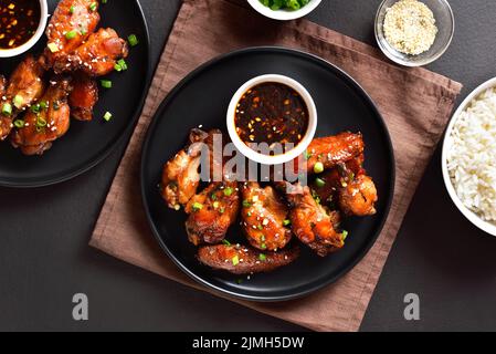 Ailes de poulet au miel et au soja collantes sur une assiette sur fond de pierre sombre. Vue de dessus, plan d'appartement Banque D'Images