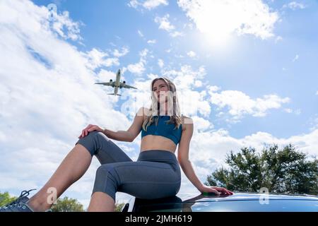 Charmante Blond Female Traveler appréciant le temps d'été comme Un avion commercial vole au-dessus de la tête Banque D'Images