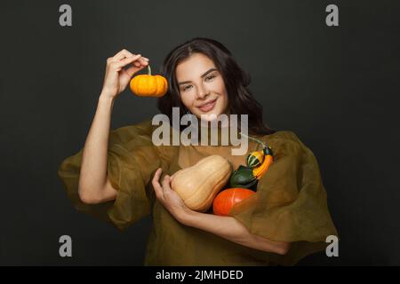 Bonne femme attrayante montrant différentes citrouilles orange et vertes sur fond noir. Portrait de Thanksgiving ou d'halloween. Banque D'Images
