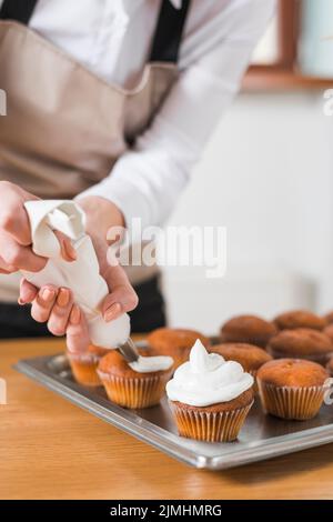 Jeune femme décorant des cupcakes avec de la crème fouettée blanche en pressant le sac de confiserie Banque D'Images