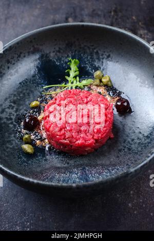 Tartre gastronomique de style moderne à base de filet de bœuf avec câpres et cerise d'amarena servi avec de la crème de truffe et de la laitue en gros plan Banque D'Images