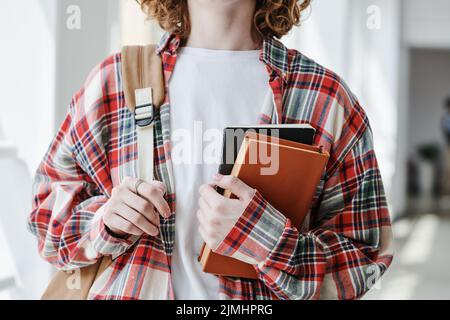 Mains de jeune étudiante féminine en t-shirt blanc et chemise à carreaux tenant un livre et un livre publicitaire tout en se tenant devant l'appareil photo Banque D'Images