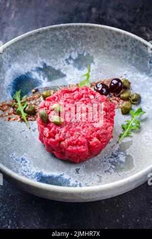 Tartre gastronomique de style moderne à base de filet de bœuf avec câpres et cerise d'amarena servi avec de la crème de truffe et de la laitue en gros plan Banque D'Images