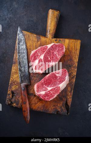 Des steaks de bœuf Angus vieilli et sec sont offerts avec vue sur un vieux panneau rustique en bois Banque D'Images