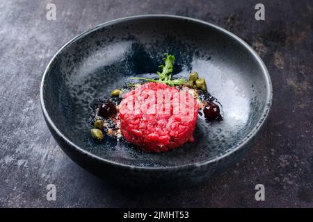 Tartre gastronomique de style moderne à base de filet de bœuf avec câpres et cerise d'amarena servi avec de la crème de truffe et de la laitue en gros plan Banque D'Images