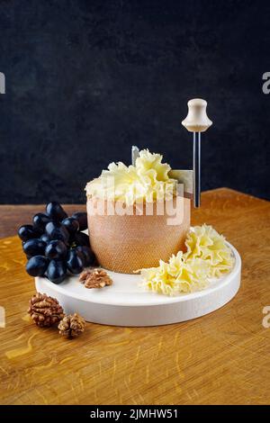 La tête de moine traditionnelle fromage de montagne des Alpes servi avec des raisins sur une girolle sur une planche de bois Banque D'Images