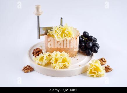 Traditionnel tete de moine vieux fromage de montagne des Alpes servi avec des raisins et des noix sur un girolle sur fond blanc Banque D'Images
