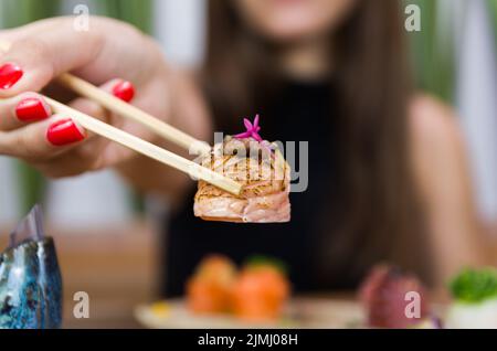 Femme mangeant de délicieux sushis, en gros plan sur des baguettes. Banque D'Images