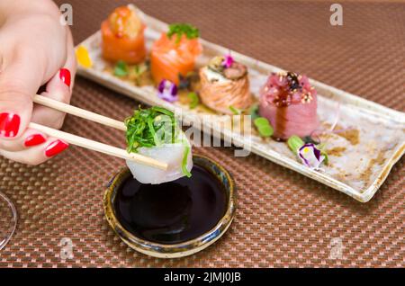 Femme mangeant de délicieux sushis, en gros plan sur des baguettes. Banque D'Images