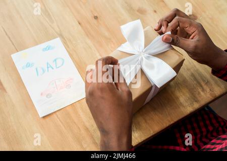 Homme dénouant la boîte cadeau de noeud près de la carte de voeux Banque D'Images