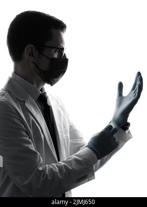 Profil du médecin caucasien portant des gants en latex, un masque et un manteau blanc isolés sur fond blanc. Portrait de silhouette avec masque de visage professionnel médical Banque D'Images