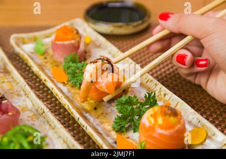 Femme mangeant de délicieux sushis, en gros plan sur des baguettes. Banque D'Images