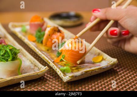 Femme mangeant de délicieux sushis, en gros plan sur des baguettes. Banque D'Images