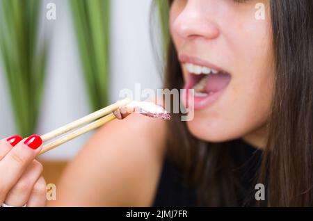 Femme mangeant délicieux sashimi, gros plan sur des baguettes. Banque D'Images