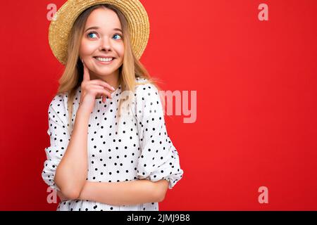 Photo portrait de jeune belle mignonne heureuse blonde femme portant une robe décontractée et chapeau de paille isolé sur fond rouge avec c Banque D'Images