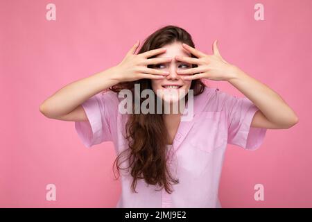 Portrait de jeune émotive positive drôle belle marrielle brune femme avec des émotions sincères portant décontracté rose chemise isolat Banque D'Images