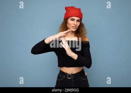 Jeune émotive insatisfaite jolie femme brunette ondulée-cheveux avec des émotions sincères portant noir crop top et Red Hat isolé Banque D'Images