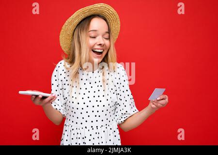Photo de jeune belle belle positive heureuse blonde femme portant une robe décontractée et chapeau de paille isolé sur fond rouge Banque D'Images