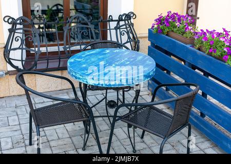 Vue sur une table vide dans un café en plein air dans la rue. terrasse de café et de restaurant avec chaises élégantes en métal, table bleue et flo Banque D'Images