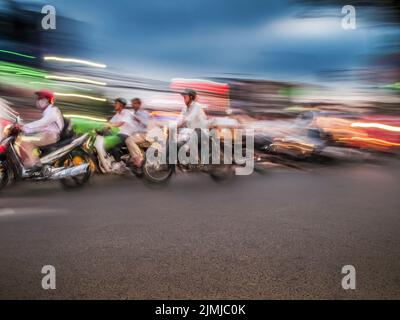 Les motocyclistes circulent dynamiquement le long d'une rue urbaine éclairée pendant le crépuscule Banque D'Images